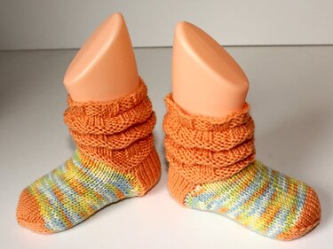 Zwei gestrickte Babysocken mit orangefarbenem Bündchen und pastellfarbenen Streifen