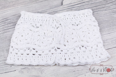 Weiße gehäkelte Baby-Shorts mit Lochmuster und Kordelbund auf hellem Holzuntergrund.