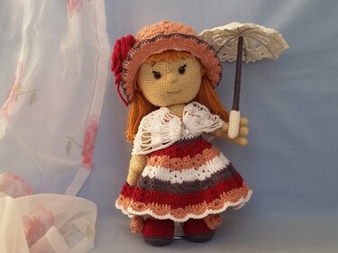 Gehäkelte Amigurumi-Puppe in gestreiftem Kleid mit Häkelhut und Spitzenparasol
