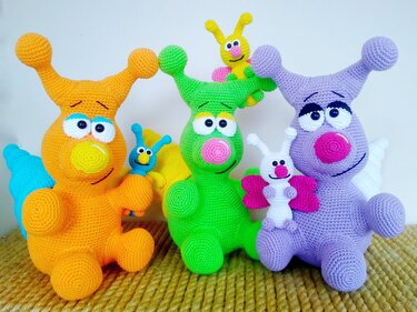 Three finished amigurumi snails in orange, green, and purple, each with a small companion figure.