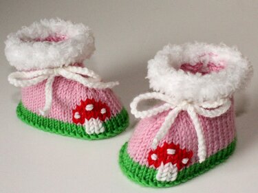 Rosa gestrickte Babyschuhe mit grünem Rand, weißem flauschigem Umschlag, Bindeband und rotem Pilzmotiv