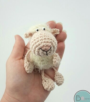 Hand hält mini gehäkeltes Amigurumi-Schaf mit flauschigem Körper und schwarzen Augen
