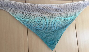 Dreieckstuch im Filethäkelmuster mit Flügelmotiv, Farbverlauf Weiß zu Türkis, aufgehängt vor Holzschrank