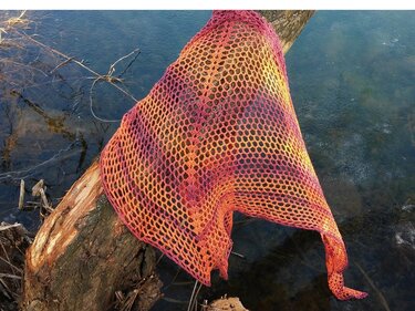 Gehäkeltes Dreieckstuch mit offenem Netzmuster in Gelb‑Orange‑Violett, über einem Baumstamm am Wasser drapiert