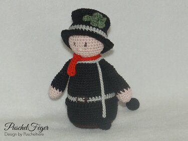 Gehäkelte Schornsteinfeger-Puppe in Schwarz mit rotem Schal, schwarzem Zylinder mit grünem Kleeblatt und kleinem Besen.