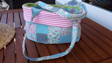 Buntes Patchwork-Utensilo mit Henkeln auf braunem Holztisch, verschiedene Stoffmuster sichtbar