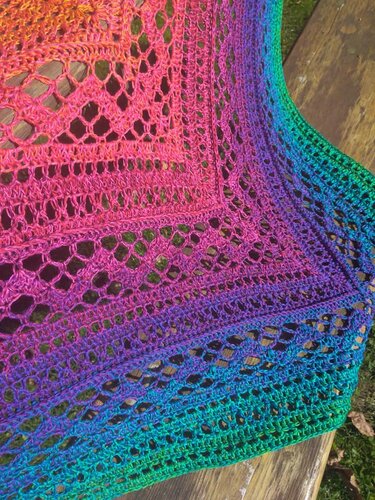 Nahaufnahme eines gehäkelten Dreieckstuchs mit Farbverlauf von Pink über Lila zu Grün und geometrischem Lochmuster.
