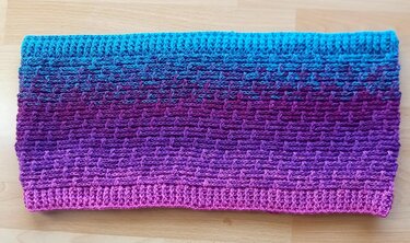 Gehäkelter Loop-Schal in Türkis, Lila und Pink, flach auf dem Tisch gelegt