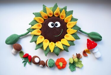 Gehäkelte Sonnenblume mit lächelndem Gesicht, darunter eine bunte Herbstgirlande mit Pilzen, Kürbis und Eicheln