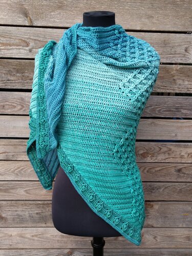 Mannequin trägt türkises gehäkeltes Dreieckstuch mit dekorativer Kante vor Holzwand