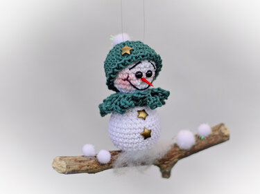 Gehäkelter weißer Schneemann mit grüner Mütze und Schal auf dekoriertem Holzast