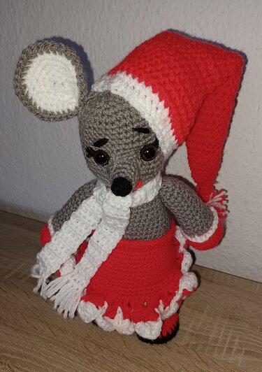Gehäkelte graue Maus mit roten Weihnachtsaccessoires: Mütze, Schal und Rock.