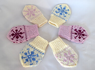 Sechs gestrickte Babyfäustlinge in Pastellfarben mit Schneeflockenmuster, im Kreis angeordnet.
