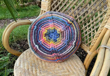 Rundes gehäkeltes Kissen mit mehrfarbigem Sternmuster auf einem Rattanstuhl