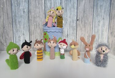 Mehrere bunte, handgehäkelte Fingerpuppen (Tiere und Märchenfiguren) vor hellem Holzpaneel.