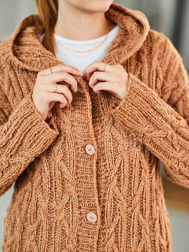 Detailaufnahme einer karamellfarbenen, grob gestrickten Damenjacke mit Kapuze und Knöpfen, Hände schließen die Knopfleiste