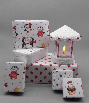 Weihnachtsgeschenke mit Pinguin- und Sternenpapier neben einer gehäkelten LED-Laterne
