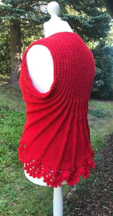 Rote gehäkelte Damenweste mit Diagonalmuster und Muschelsaum auf weißer Schneiderpuppe im Garten