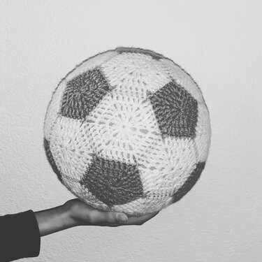 Hand hält einen gehäkelten Fußball aus Garn mit Fünf- und Sechseckfeldern