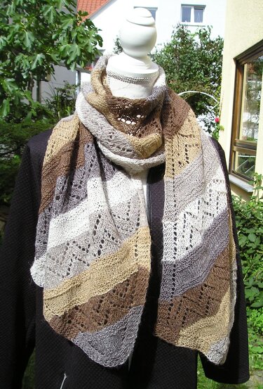 Gestrickter Schal in Erdtönen mit diagonalen Streifen und zartem Lochmuster an einer Schaufensterpuppe.