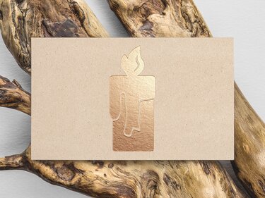 Kerzenmotiv in kupferfarbener Folienprägung auf beigem Kraftpapier, arrangiert mit Treibholz.