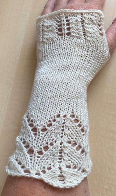 Cremefarbene, handgestrickte Armstulpe mit Lochspitzenmuster an Bündchen und oberer Kante, getragen am Unterarm
