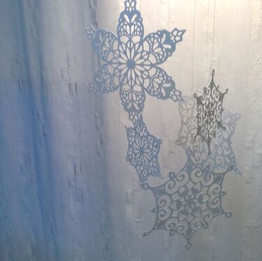 Filigrane Schneeflocken-Ornamente hängen vor einem hellen Vorhang.