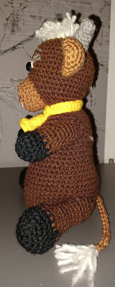 Seitliches Profil einer braunen gehäkelten Amigurumi-Kuh mit gelbem Schal