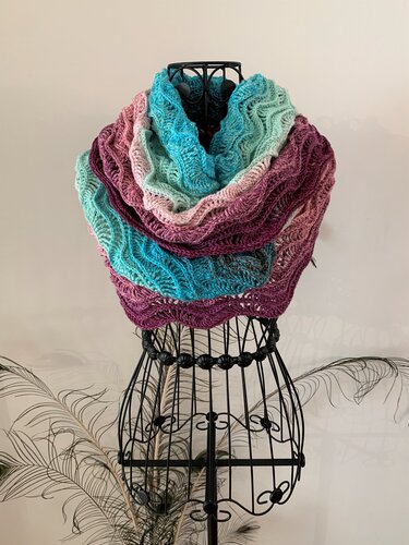 Crocheted cowl in teal, pink, and plum with a wavy ripple stitch on a wire mannequin.
