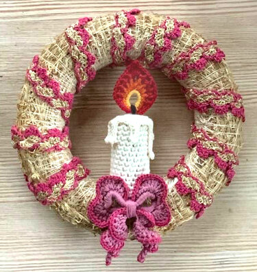Strohring mit rosa-goldener gehäkelter Zickzack-Borte, weißer gehäkelter Kerze mit Flamme und rosa Häkel-Schleife