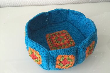 Runder gehäkelter Korb aus bunten Granny-Squares mit türkiser Umrandung