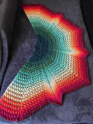 Crochet gradient shawl laid flat showing teal center fading to cream, orange and magenta with pointed scalloped edges