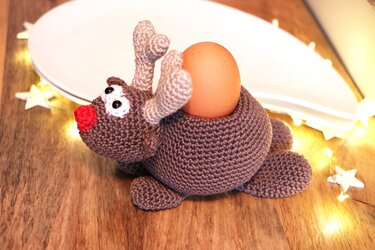 Gehäkeltes Rentier mit roter Nase als Eierhalter neben Lichterkette