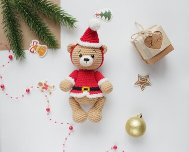 Gehäkelter Amigurumi-Teddy im roten Weihnachtsoutfit mit Geschenk, Kugel und Tannenzweig