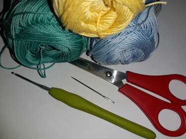 Bunte Garnknäuel neben Häkelnadel, Stopfnadel und Schere
