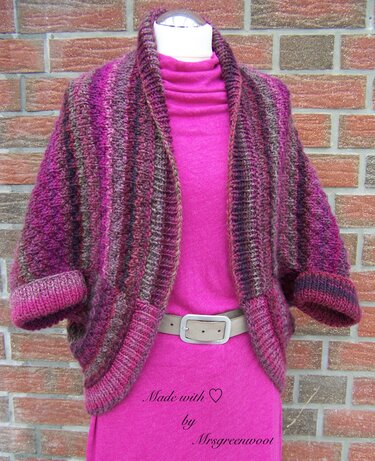 Gestrickter kurzgeschnittener Seelenwärmer in Pink- und Beerenstreifen auf Schaufensterpuppe vor Backsteinwand