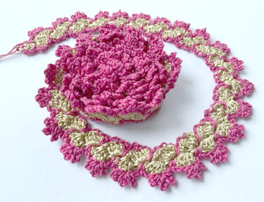 Gehäkelte Dekoration in Rosa und Beige auf weißem Hintergrund