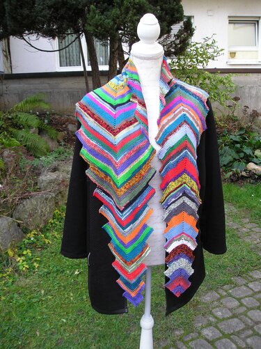 Mehrfarbiger gestrickter Drachenschwanz-Schal mit Zickzackmuster auf einer weißen Schneiderpuppe im Garten.