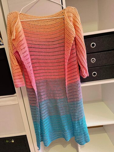 Lange gehäkelte Damenjacke mit Farbverlauf in Pfirsich, Rosa, Lila und Türkis an einem Kleiderbügel