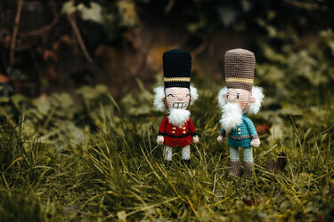 Zwei gehäkelte Amigurumi-Nussknacker in roten und türkisfarbenen Uniformen auf Gras