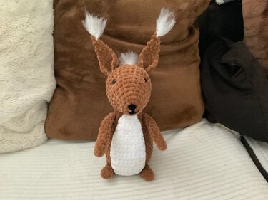 Gehäkeltes braunes Amigurumi-Tier mit weißem Bauch und Puschelohren, frontal