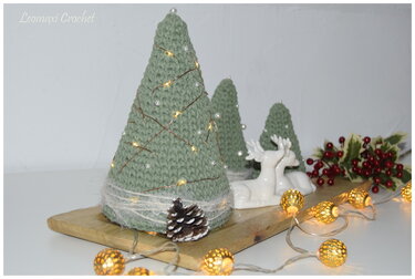 Nahaufnahme selbstgemachter Weihnachtsdekoration mit gehäkelten Bäumen, Lichterkette, Deko-Rehen und Tannenzapfen auf einem Holztablett