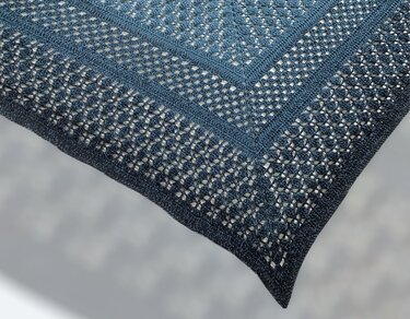 Close-up of a dark blue crocheted triangle shawl with open lace pattern and solid borders.