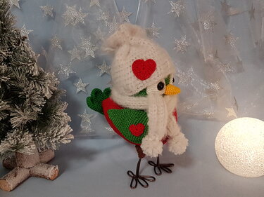 Gehäkelter Amigurumi-Vogel mit weißer Mütze und Schal, roten Herz-Applikationen, Drahtbeinen und winterlicher Dekoration