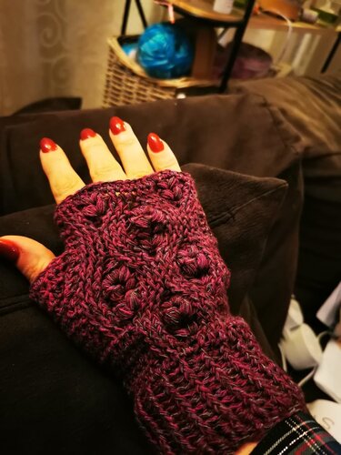 Hand mit fingerloser gehäkelter Stulpe in Pflaume mit Noppen- und Rautenrelief