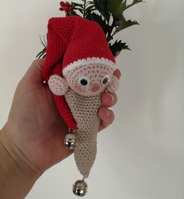 Gehäkelter Wichtel mit roter Zipfelmütze, Wackelaugen und Glöckchen, gehalten in einer Hand