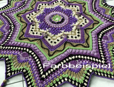 Nahaufnahme einer gehäkelten sternförmigen Decke in Violett, Grün, Beige und Schwarz mit komplexem Muster und Wasserzeichen 'Farbbeispiel'.