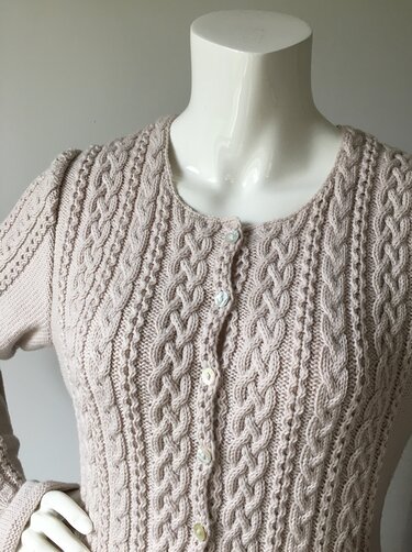 Mannequin wearing pale neutral cable-knit women's button-up cardigan with braided cables and crew neck