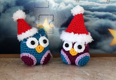 Zwei bunte Amigurumi-Eulen mit roten Weihnachtsmützen