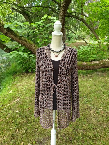 Braun-melierter gehäkelter Damen-Cardigan mit Lochmuster und schmalem Bindeband auf einer Schneiderpuppe vor grünem Hintergrund.